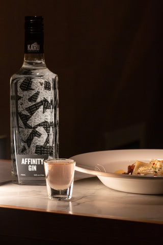 Bottle of Affinity Gin with a glass of gin and tonic on a table.